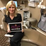 Staff memer smiling and sitting at dental chair. She is holding a plate with inscription: "Queen of oral hygiene".