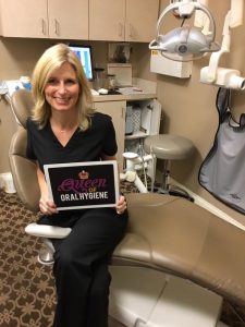 Staff memer smiling and sitting at dental chair. She is holding a plate with inscription: "Queen of oral hygiene".