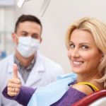 A satisfied smiling woman in a dental chair showing her thumb up.
