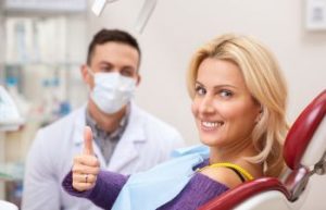 A satisfied smiling woman in a dental chair showing her thumb up.