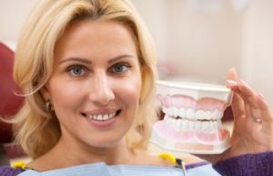 A smiling woman with a dental model sitting in a dental chair.