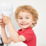 smiling boy in the dental office holding a big toy tooth