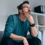Shot of worried mature man thinking about what he has read on his mobile phone while sitting on the couch at home
