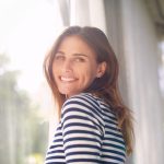 Woman, smile and portrait in house for relax and calm for holiday and cheerful on blurred background. Young person and happy with window for view of garden or backyard with sunlight in lounge