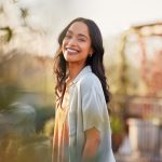Young latin woman in casual clothing in the garden looking at camera, during early morning. Portrait of healthy mexican girl enjoying nature during sunset. Mindful multiethnic woman enjoy morning ritual with fresh air.